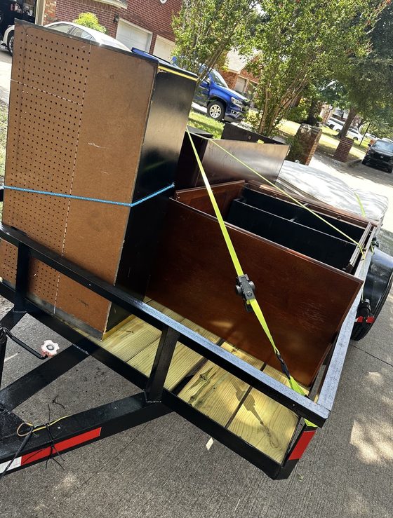 Trailer loaded with a dresser, cabinets and shelving units strapped down in a residential driveway