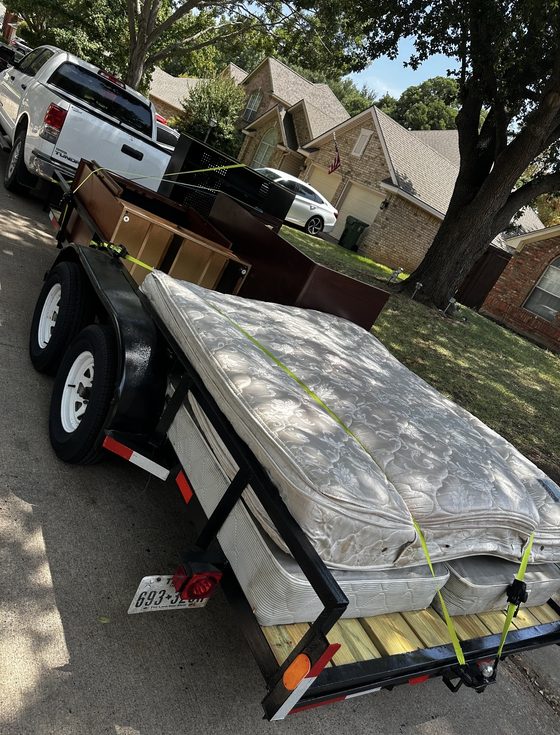Two mattresses and wooden furniture loaded and ratchet-strapped on the Z&M trailer on a suburban street